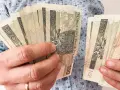 Ręce trzymające stos banknotów 100 zł. Zastanawiasz się, kiedy najlepiej przejść na emeryturę w 2026 roku?