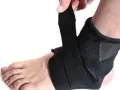 Dłoń zapina czarną ortezę na stopę, zapewniając wsparcie i stabilizację.
