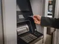 Dłoń wsuwa kartę do bankomatu, by sprawdzić, ile można wypłacić.