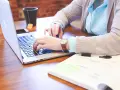 Kobieta pracuje na laptopie, analizując dokumenty. Może to być związane z rozliczeniem podatku od wzbogacenia.