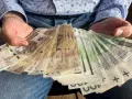 Ręce trzymające stos banknotów, w tym 1000 plus złotych. Widać portret Kopernika na jednym z banknotów.