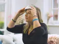 Kobieta w czarnej bluzce zakłada na głowę urządzenie tianesal. Ma na rękach bransoletki i niebieską opaskę.