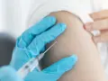 Ręka w niebieskiej rękawiczce podaje szczepionkę na kleszcze. Zabezpiecz się przed boreliozą i kleszczowym zapaleniem mózgu.