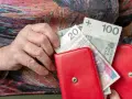 Dłoń starszej osoby wkłada banknoty 20 i 100 zł do czerwonego portfela. Czerwcowe emerytury wreszcie dotarły.