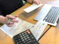 Ręka z długopisem nad dokumentami ZUS, obok kalkulator i laptop. Przygotowanie do wniosku o emeryturę pomostową.