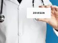 Lekarz w białym kitlu trzyma kartkę z napisem ZEVEISIN. Stetoskop wisi na jego szyi.