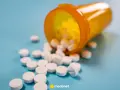 Białe tabletki rozsypane z pomarańczowego pojemnika. Mogą to być leki immunosupresyjne, które pomagają w transplantacjach.