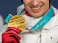 Uśmiechnięty sportowiec w czerwonej rękawicy trzyma złoty medal olimpijski z PyeongChang. Taki medal to marzenie o emeryturze.