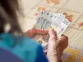 Dłonie starszej osoby liczą banknoty 200 zł. Może to symbolizować drugą waloryzację emerytur i wzrost dochodów.