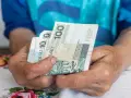 Dłonie starszej osoby trzymają banknoty 100 zł. Czy to wystarczy na godne życie, gdy średnia emerytura w Polsce jest taka, jaka jest?