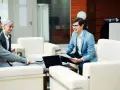 Trzy osoby w garniturach omawiają dokumenty, planując zakup mieszkania bez wkładu własnego.