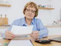 Zmartwiona kobieta w okularach analizuje dokumenty, zastanawiając się, ile lat pracy do emerytury jej pozostało.