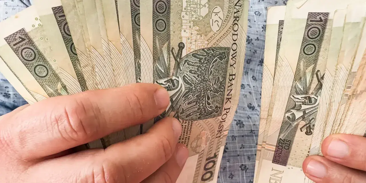 Ręce trzymające stos banknotów 100 zł. Zastanawiasz się, kiedy najlepiej przejść na emeryturę w 2026 roku?
