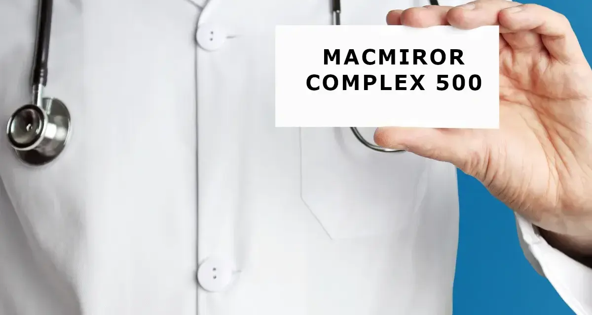 Lekarz w białym kitlu trzyma kartkę z napisem MACMIROR COMPLEX 500. Stetoskop wisi na jego szyi.