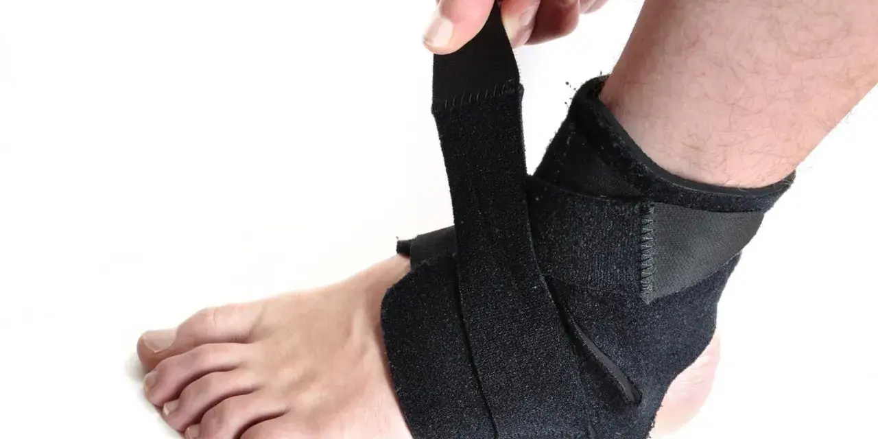 Dłoń zapina czarną ortezę na stopę, zapewniając wsparcie i stabilizację.