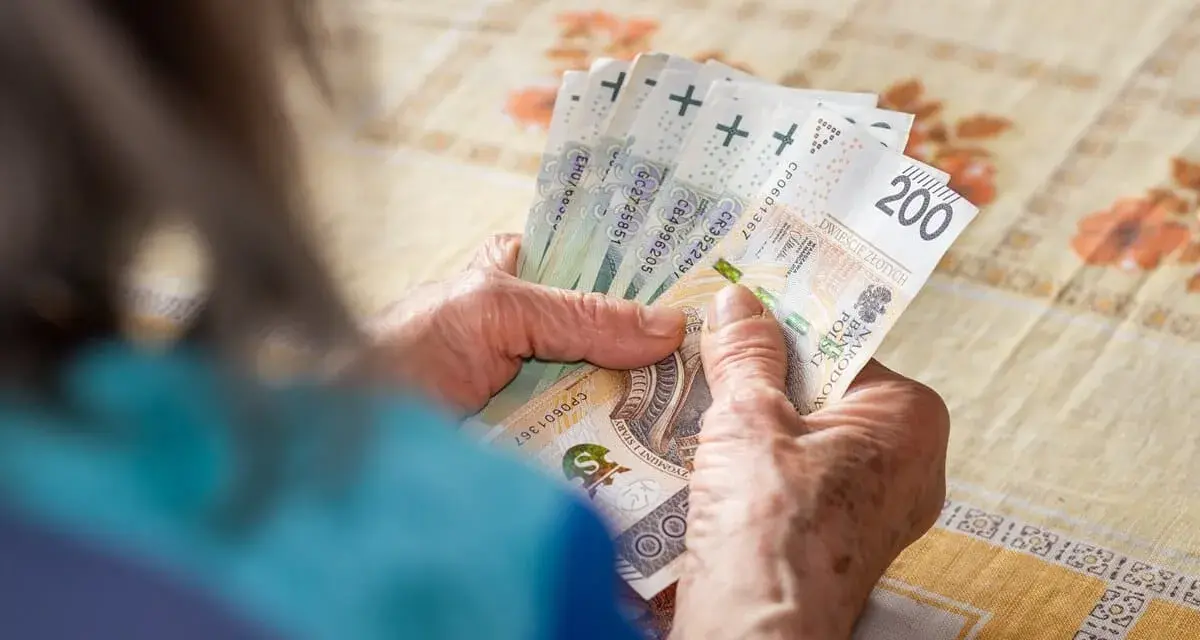 Dłonie starszej osoby liczą banknoty 200 zł. Tabela 13 emerytura 2026 może zawierać podobne kwoty.