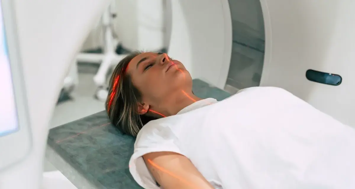 Kobieta leży na łóżku w aparacie do rezonansu magnetycznego. Czerwone linie lasera wskazują obszar badania. To właśnie mri co to za badanie?