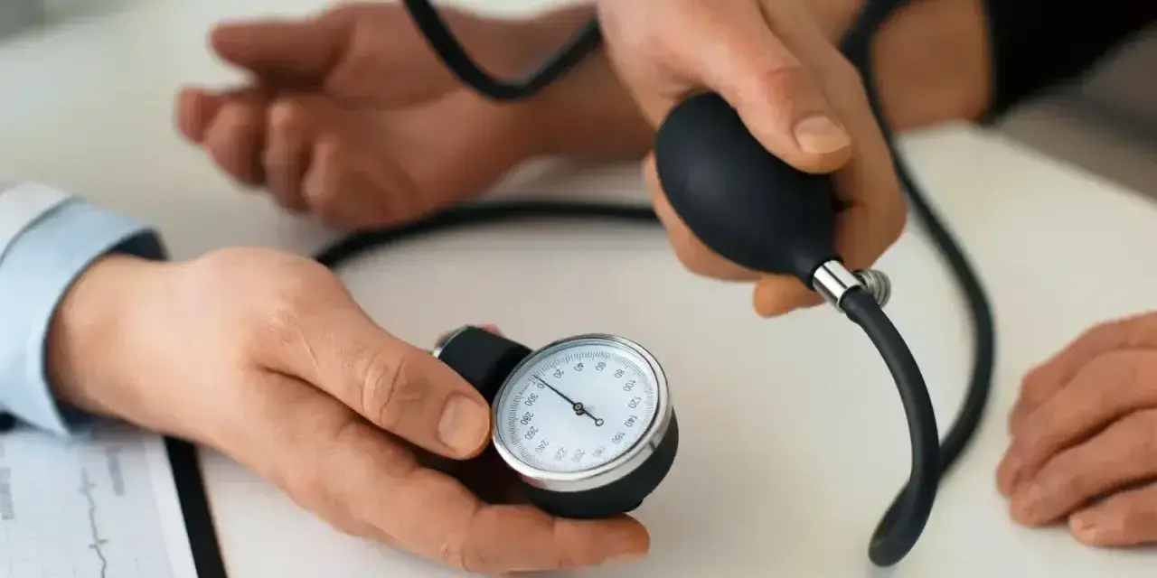 Lekarz mierzy ciśnienie krwi pacjentowi. Na stole leży ciśnieniomierz, a obok dokument z zapisem EKG. To ważny element profilaktyki, dbanie o prenessa jest kluczowe.