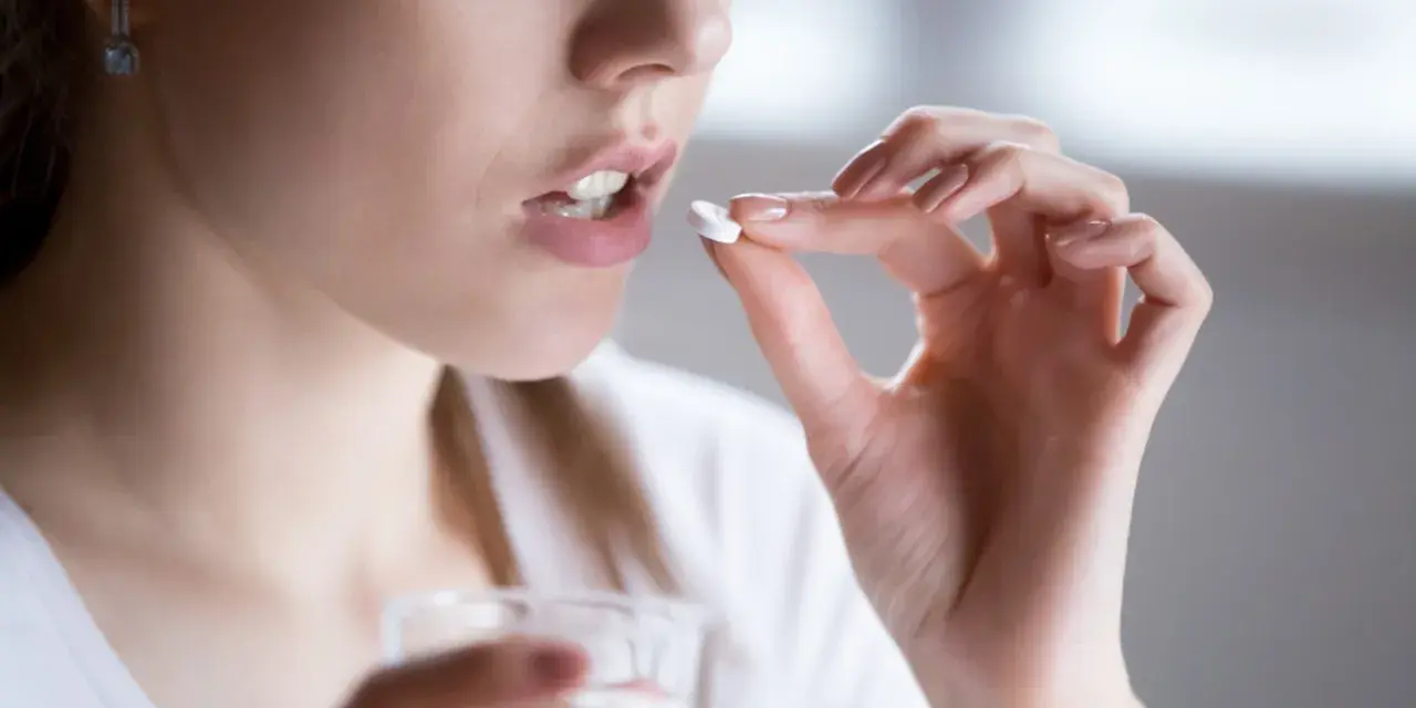 Kobieta bierze tabletkę clindamycin mip 600, trzymając szklankę wody.