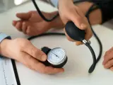 Lekarz mierzy ciśnienie krwi pacjentowi. Na stole leży ciśnieniomierz, a obok dokument z zapisem EKG. To ważny element profilaktyki, dbanie o prenessa jest kluczowe.