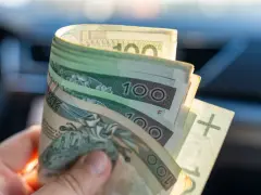 Dłoń trzyma zwitek polskich banknotów 100 zł. Dokument orzeczenie o niepełnosprawności może pomóc w uzyskaniu zasiłek pielęgnacyjny.
