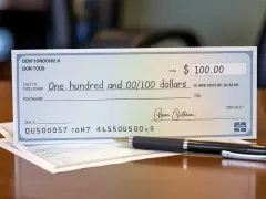 Czek na sto dolarów leży na biurku obok długopisu.