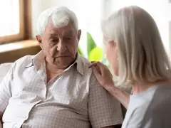 Starszy mężczyzna z zamyśloną miną, kobieta kładzie mu dłoń na ramieniu. Może to być wsparcie w trudnych chwilach, gdy pojawiają się psychoza objawy.