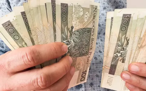 Ręce trzymające stos banknotów 100 zł. Zastanawiasz się, kiedy najlepiej przejść na emeryturę w 2026 roku?