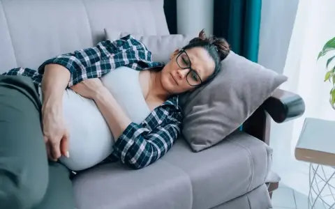 Kobieta w ciąży leży na kanapie, cierpiąc z powodu objawów przypominających listeriozę.