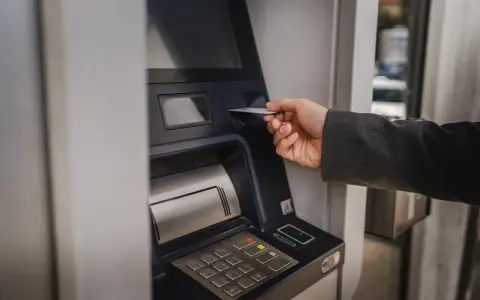Dłoń wsuwa kartę do bankomatu, by sprawdzić, ile można wypłacić.