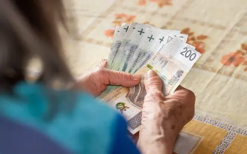 Dłonie starszej osoby liczą banknoty 200 zł. Tabela 13 emerytura 2026 może zawierać podobne kwoty.