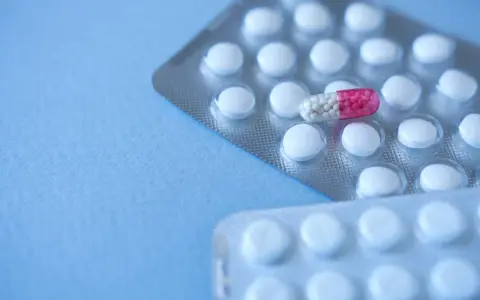 Dwie blistry z białymi tabletkami i jedną kapsułką z różowymi granulkami. Aposerta leży na wierzchu.