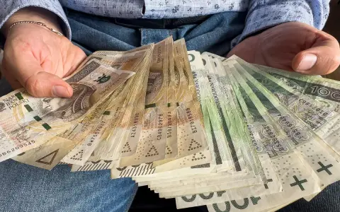 Ręce trzymające stos banknotów, w tym 1000 plus złotych. Widać portret Kopernika na jednym z banknotów.