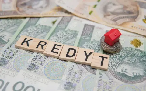 Litery układające słowo "KREDYT" na banknotach. Mały czerwony domek na stosie monet symbolizuje pomoc w spłacie kredytu, np. z funduszu wsparcia kredytobiorców.