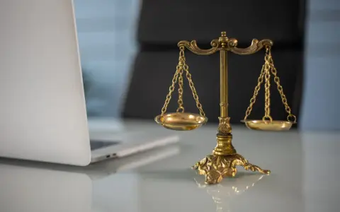 Złota waga sprawiedliwości obok laptopa. Czy to symbol obrony przed pomówieniem, czy dowód na jego istnienie?