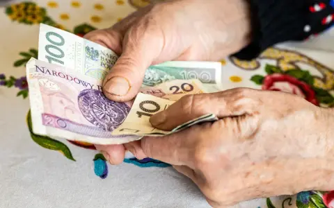 Dłonie starszej osoby liczą pieniądze. Może to być dodatek opiekuńczy po 80 roku życia, zapewniający wsparcie finansowe.