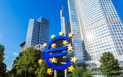 Symbol euro przed nowoczesnymi wieżowcami, siedziba europejskiego banku centralnego.