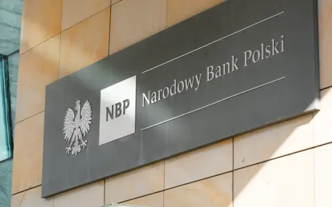 Tablica z godłem Polski i napisem "NBP Narodowy Bank Polski". Decyzje NBP wpływają na obniżkę stopy procentowej.