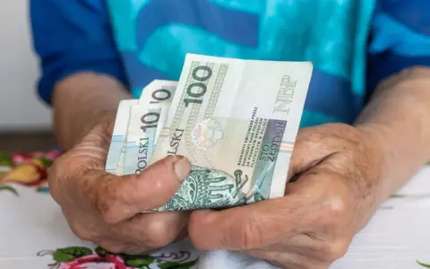 Dłonie starszej osoby trzymają banknoty 100 zł. Czy to wystarczy na godne życie, gdy średnia emerytura w Polsce jest taka, jaka jest?