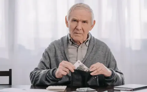 Zmartwiony starszy mężczyzna wkłada pieniądze do portfela, planując wcześniejszą emeryturę.