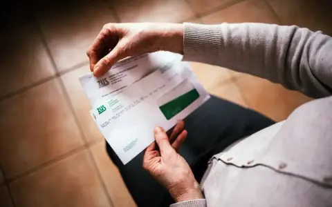 Dłonie trzymają kopertę ZUS. W środku dokumenty dotyczące 13 emerytury netto.
