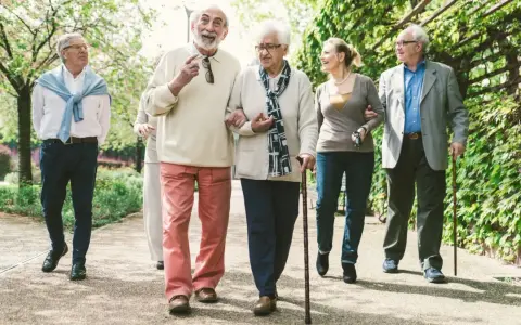 Grupa seniorów spaceruje po parku, ciesząc się świeżym powietrzem. Może rozmawiają o tym, jak przyjemnie jest płacić opłatę klimatyczną za takie widoki.