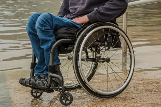 Osoba na wózku inwalidzkim, oczekująca na zus świadczenie wspierające, siedzi przy wodzie.