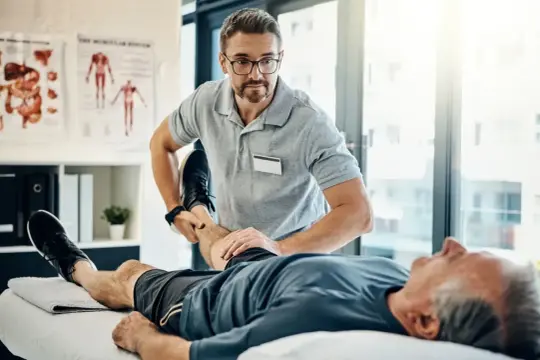 Fizjoterapeuta wykonuje ćwiczenia z pacjentem, pomagając mu w powrocie do sprawności. To profesjonalne świadczenie rehabilitacyjne.