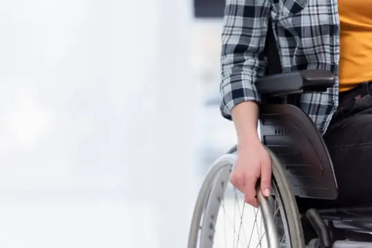 Osoba na wózku inwalidzkim, czekająca na przyznanie renty socjalnej, trzyma dłoń na obręczy koła.
