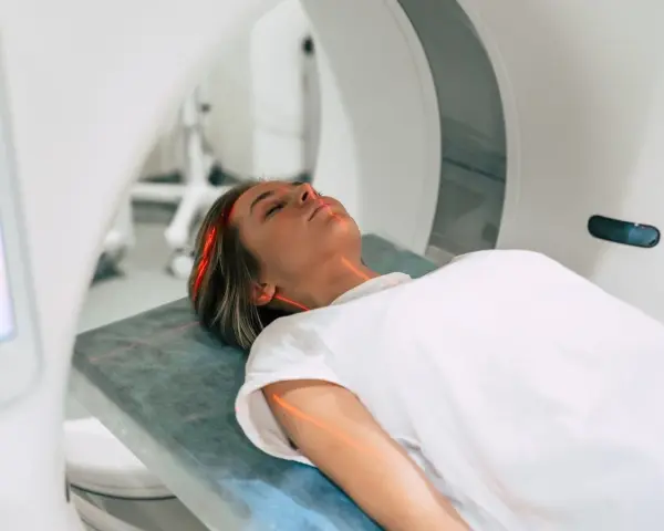 Kobieta leży na łóżku w aparacie do rezonansu magnetycznego. Czerwone linie lasera wskazują obszar badania. To właśnie mri co to za badanie?