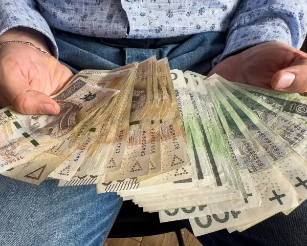 Ręce trzymające stos banknotów, w tym 1000 plus złotych. Widać portret Kopernika na jednym z banknotów.