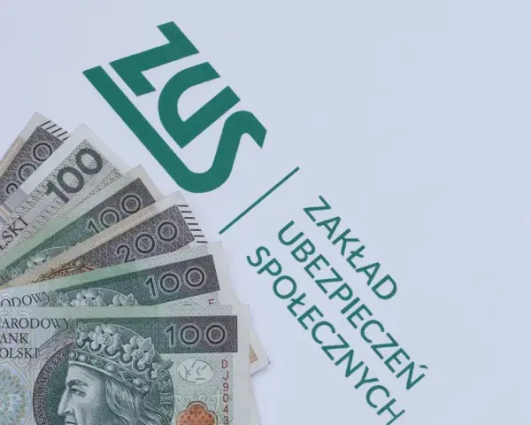 Pieniądze, w tym banknoty 100 i 200 zł, leżą obok zielonego logo ZUS. To dodatek dopełniający do świadczeń.