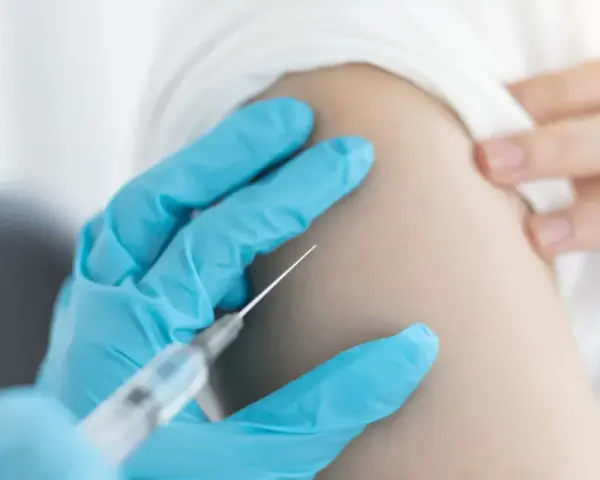 Ręka w niebieskiej rękawiczce podaje szczepionkę na kleszcze. Zabezpiecz się przed boreliozą i kleszczowym zapaleniem mózgu.