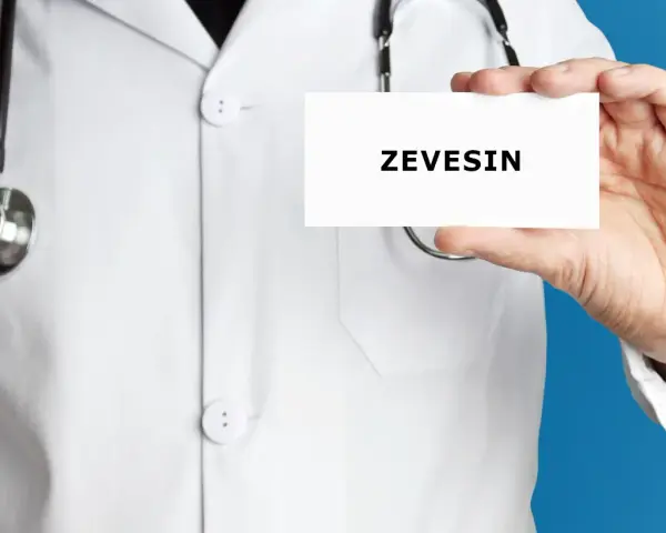 Lekarz w białym kitlu trzyma kartkę z napisem ZEVEISIN. Stetoskop wisi na jego szyi.